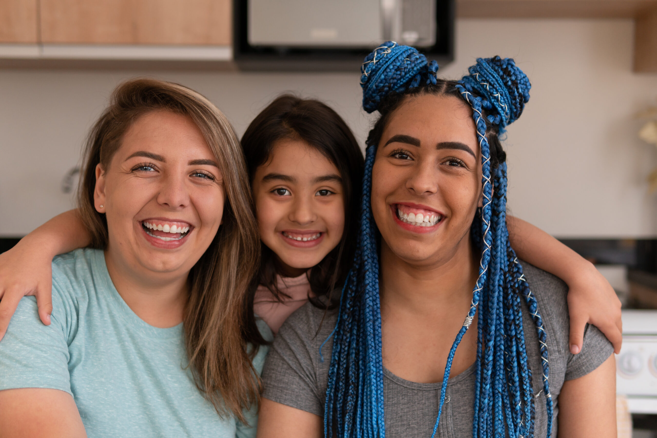 Portrait of brazilian gay couple with daughter looking at camera in kitchen home, indoors.