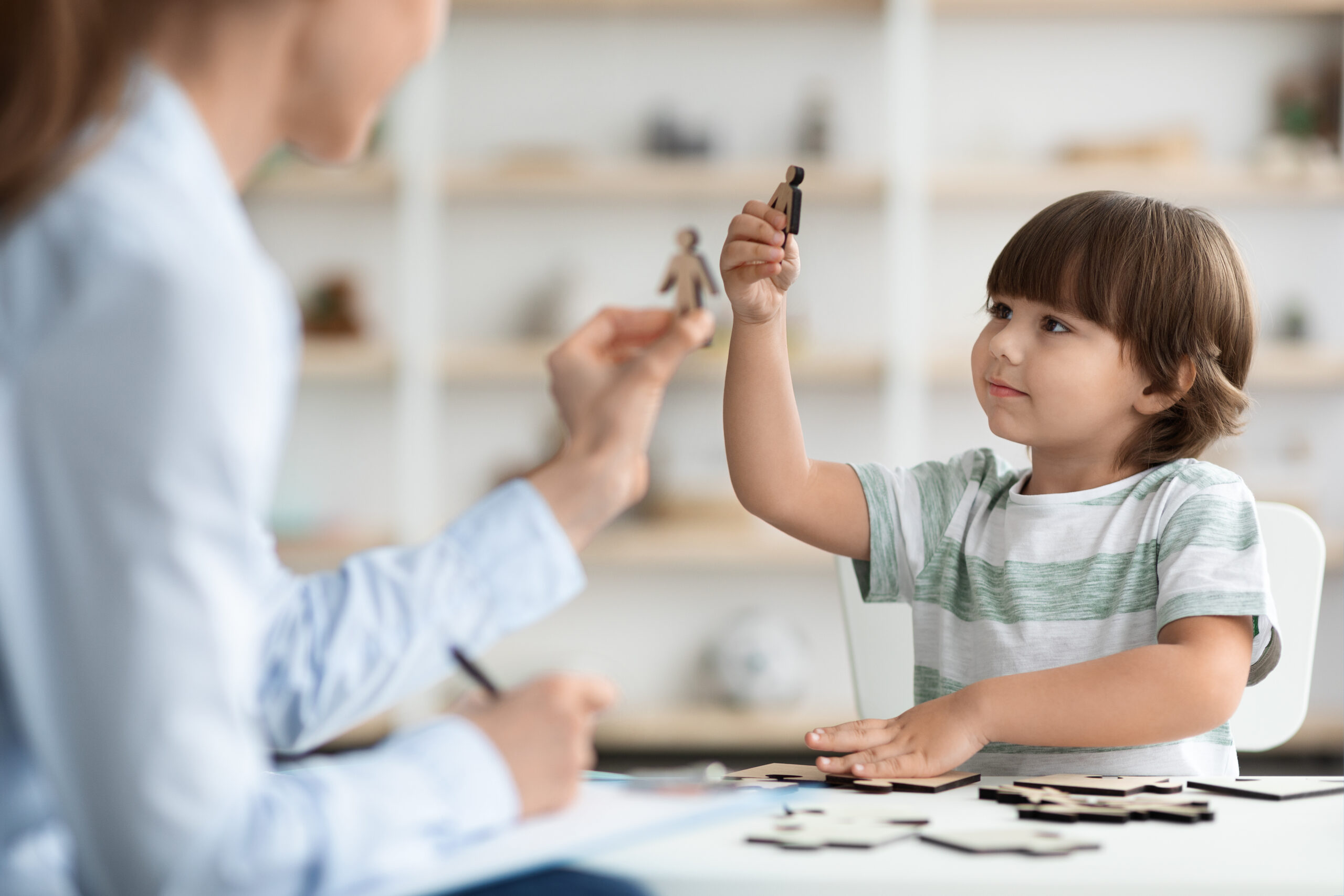 Little boy with communication problems playing with wooden figures with professional children psychologist at office